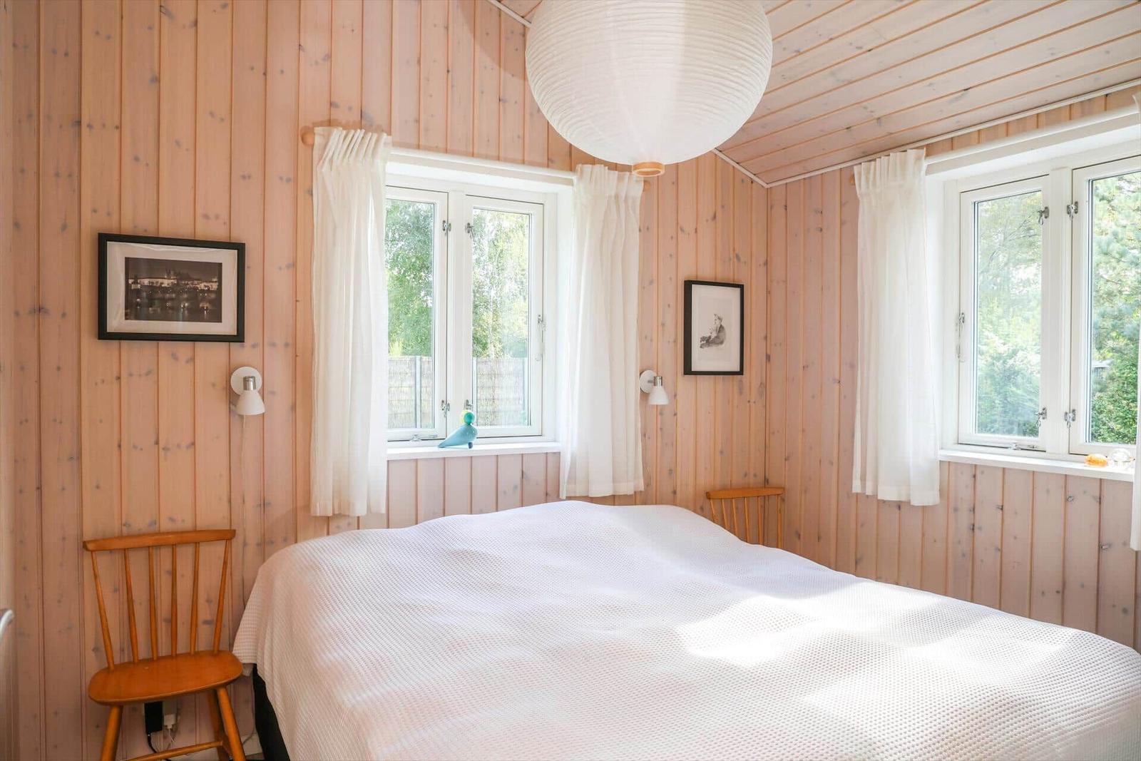Schlafzimmer mit Holzwand, Bett, Fenstern und Lampen.