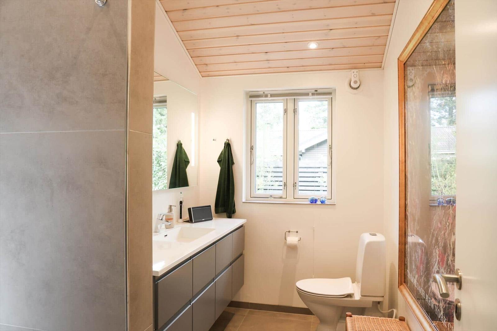 Badezimmer mit Dusche, Waschbecken und Toilette. Holzdecke und Fenster.