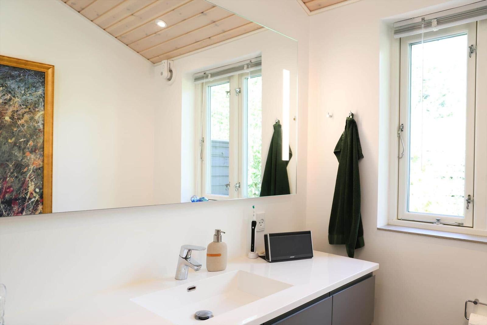 Badezimmer mit Waschbecken, Spiegel und Fenster. Handtuch hängt an Wand.