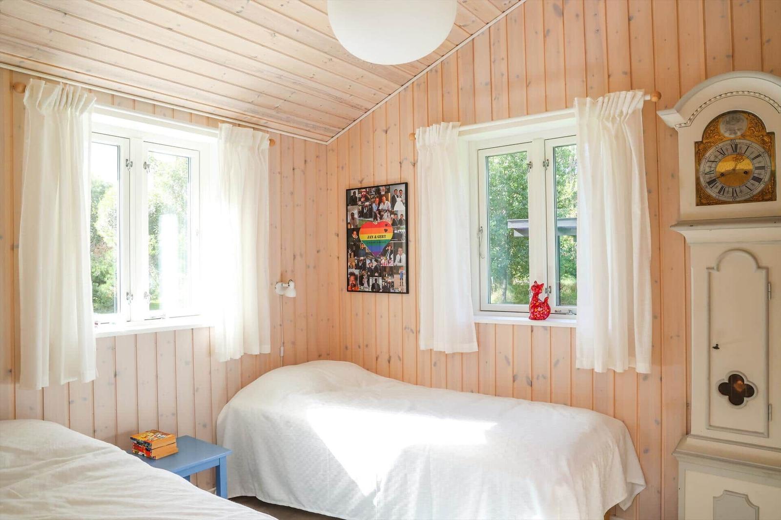 Zimmer mit zwei Betten, Holzwandverkleidung, zwei Fenstern und einer Wanduhr.