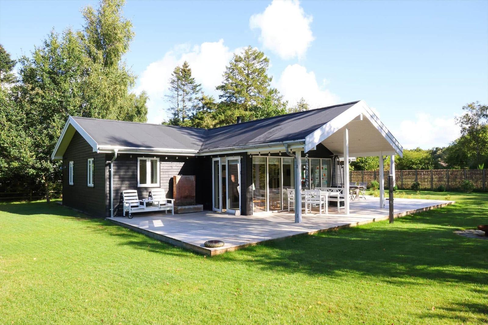 Moderne Holzhütte mit Terrasse, Garten und Grillplatz. Grosse Fenster und offene Küche.