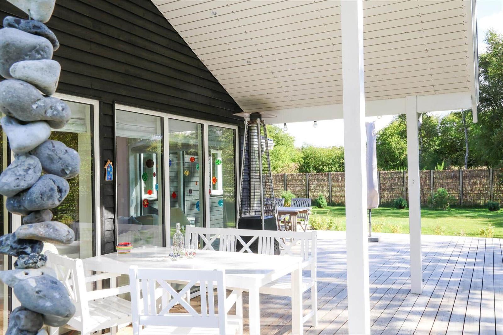 Terrasse mit weißem Tisch und Stühlen, Gasheizung und Steinpyramide. Hintergrund: Garten mit Zaun.