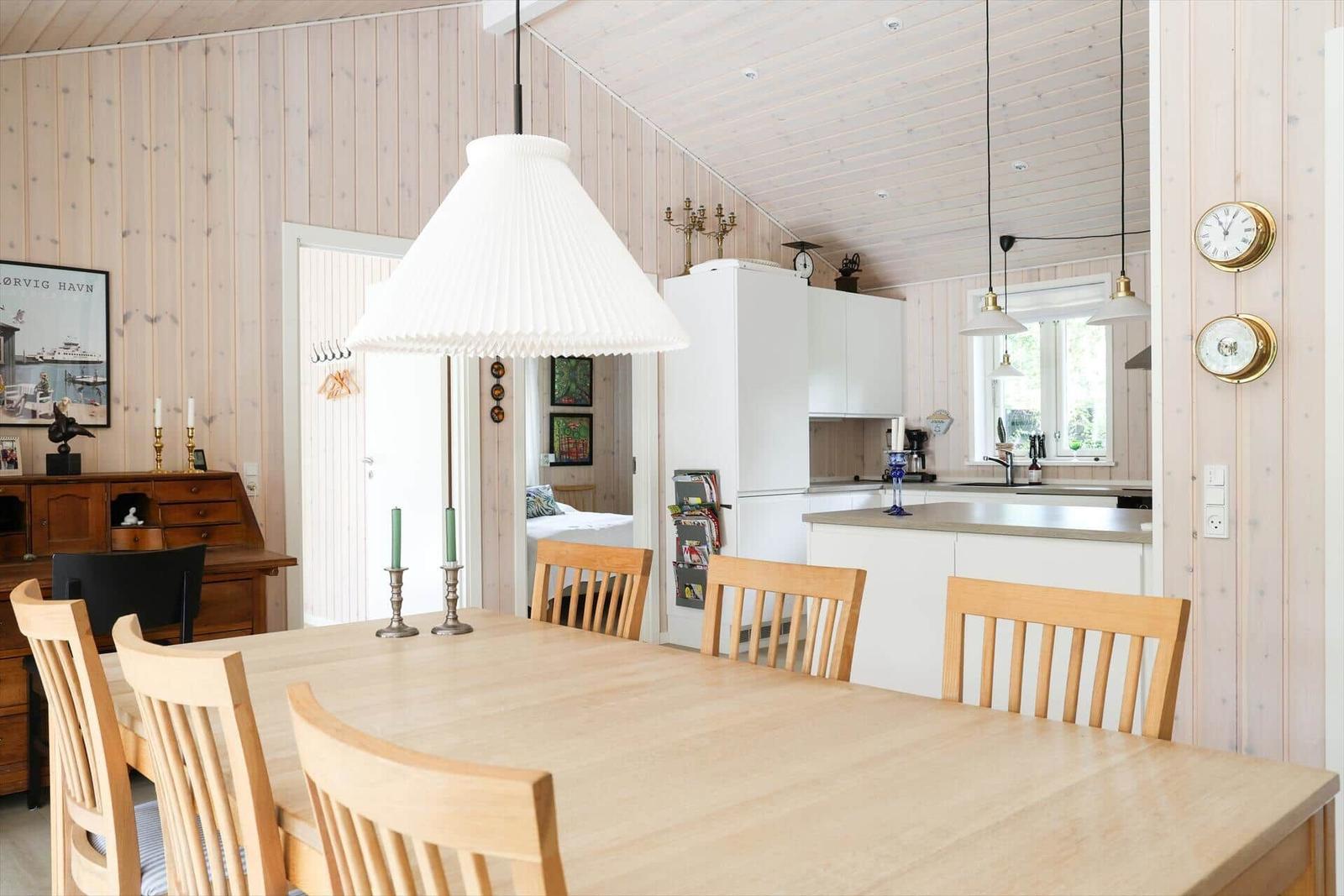 Essbereich mit Holztisch und Stühlen. Küche mit Arbeitsplatte und Fenster. Holzwand und Decke.