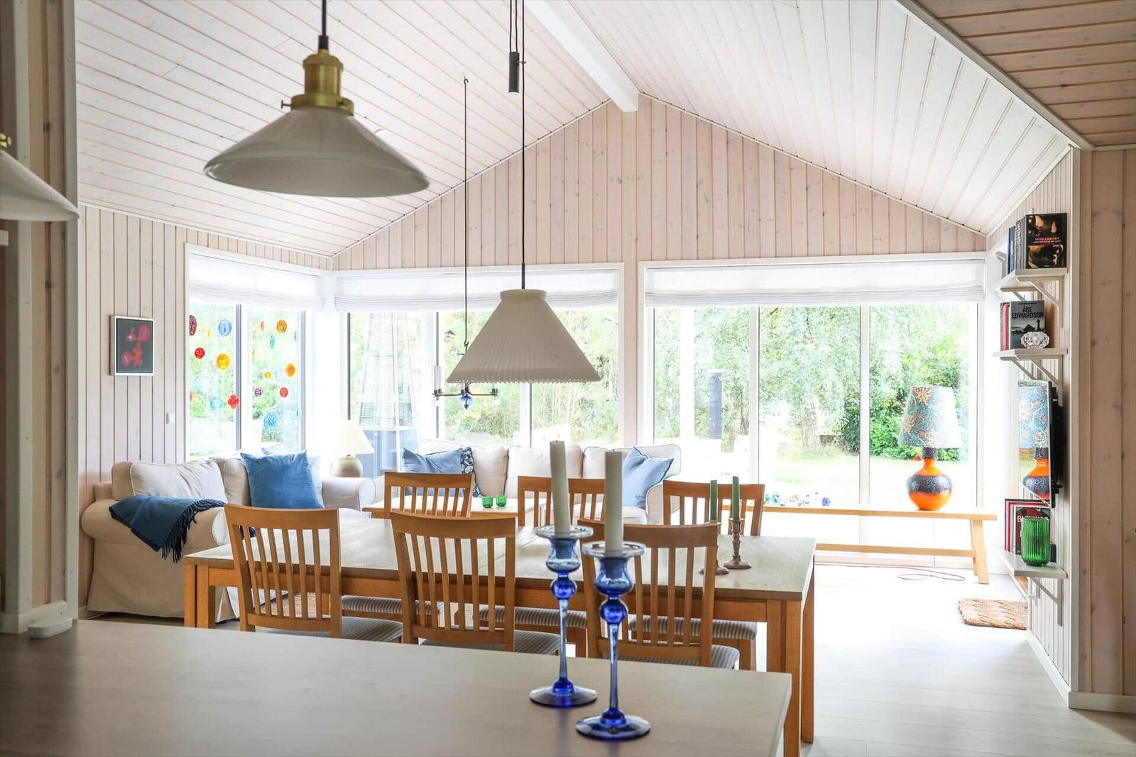 Wohn- und Essbereich mit Holzwand, Fenstern und Tisch mit Stühlen.