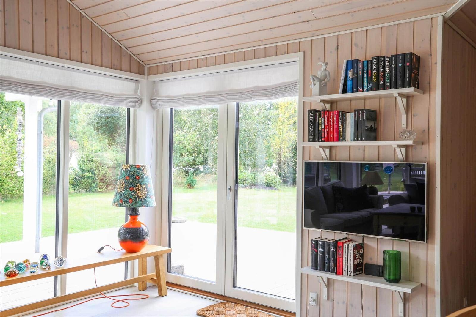 Raum mit Holzwand, großen Fenstern und Bücherregal mit Fernseher.