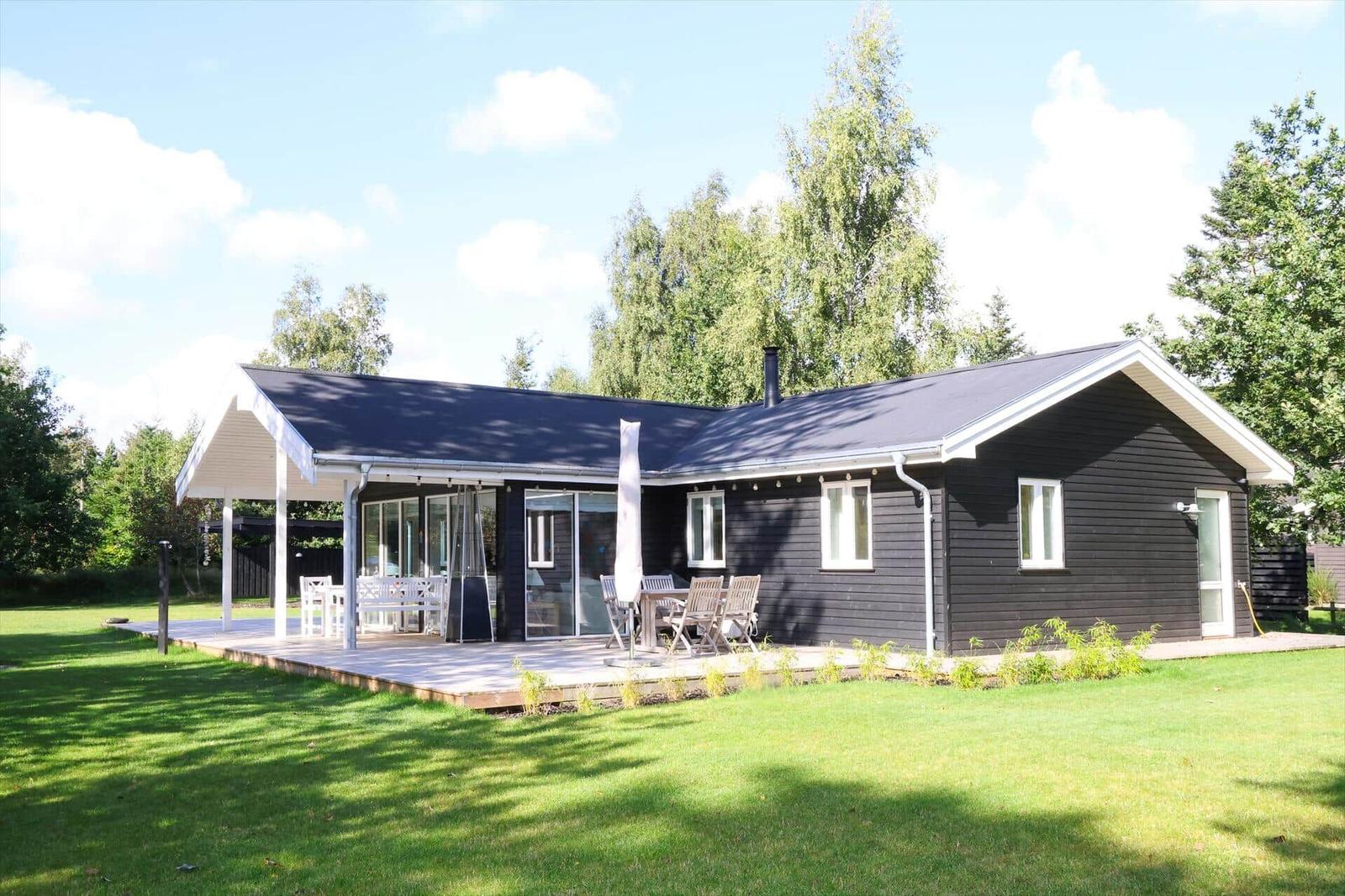 Schwarze Holzhütte mit Terrasse, Garten und Bäumen im Hintergrund.