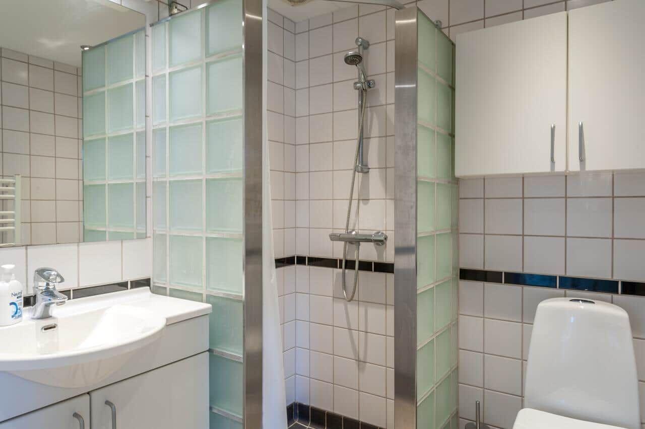 Badezimmer mit Dusche, Waschbecken und Toilette. Fliesenwand und Glaswand.