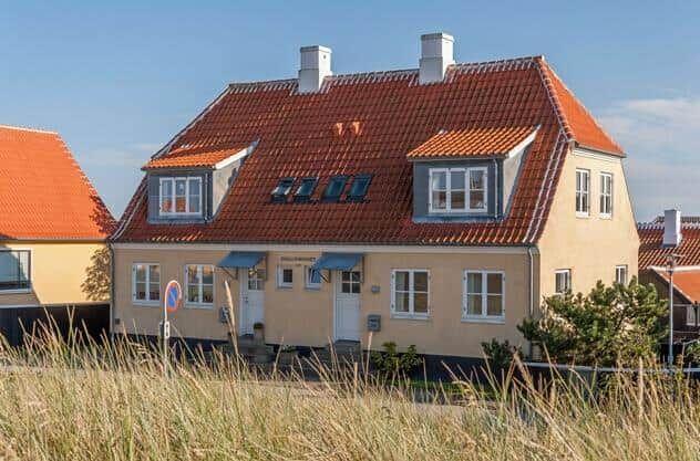 Ein zweistöckiges Haus mit rotem Dach und weißen Fenstern steht unter blauem Himmel.