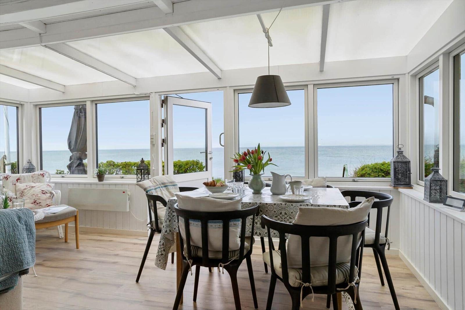 Esszimmer mit Tisch, Stühlen und Meerblick durch große Fenster.