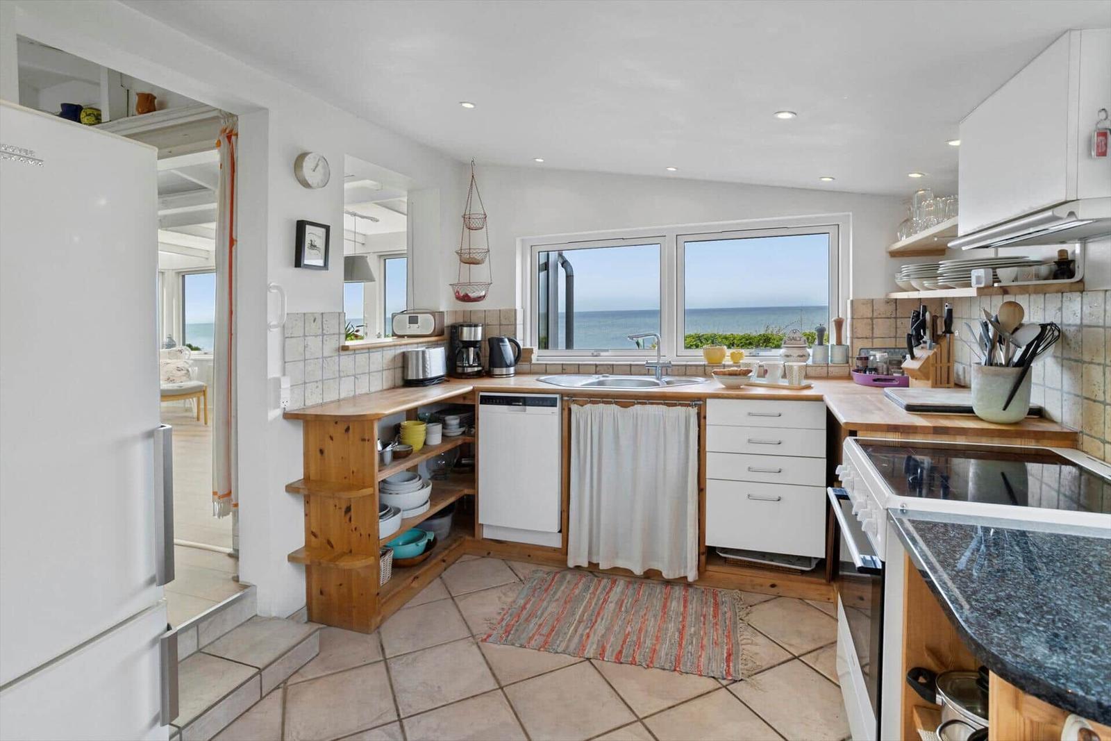 Küche mit Küchenzeile, Blick aufs Meer, Spüle, Dunstabzug und Kühlgerät.