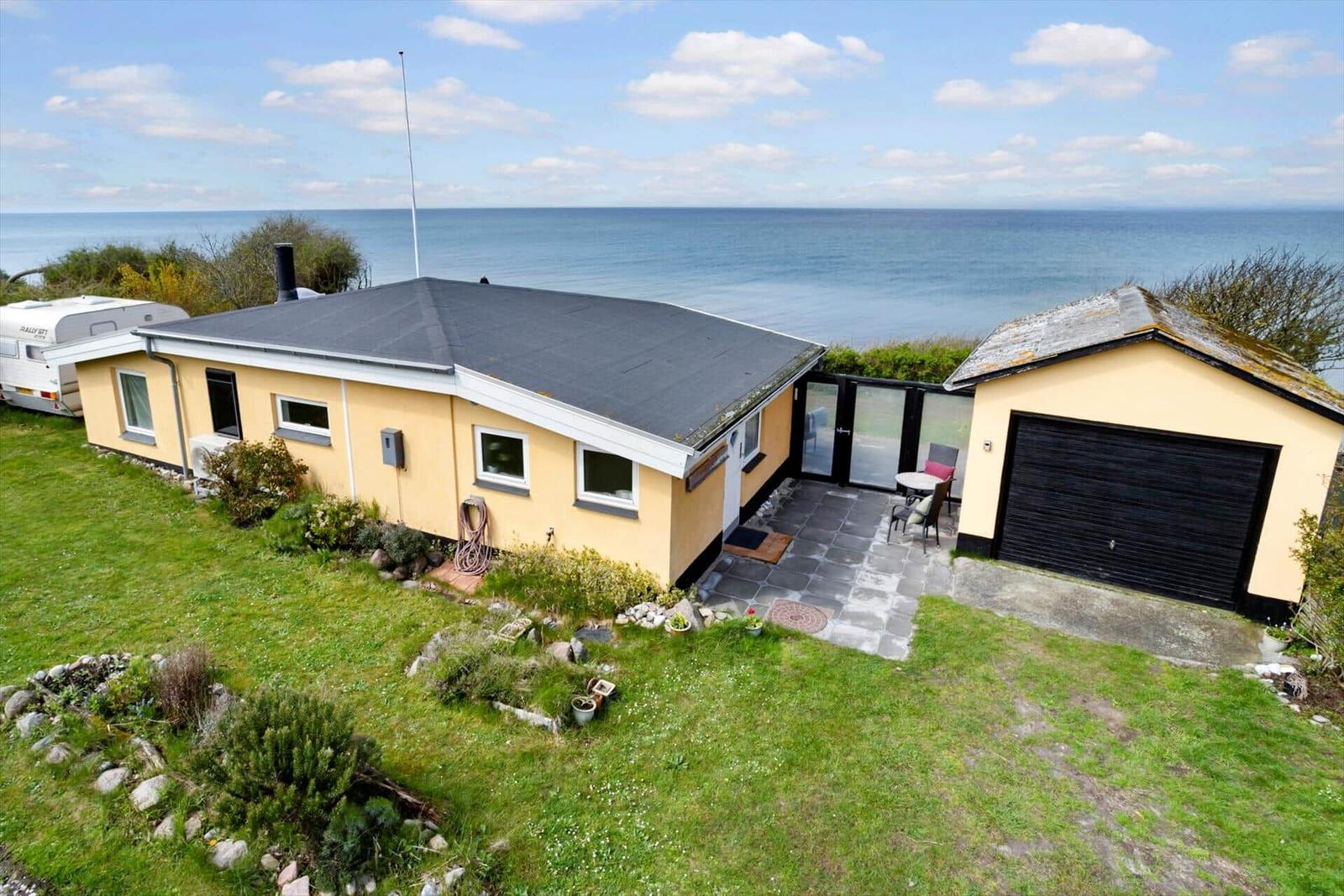 Haus mit Garten und Meerblick. Nebenhaus mit Garage. Terrasse mit Tisch und Stühlen.