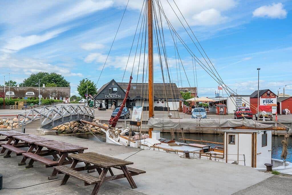 Hafen mit Segelboot, Picknicktischen und Gebäuden im Hintergrund.