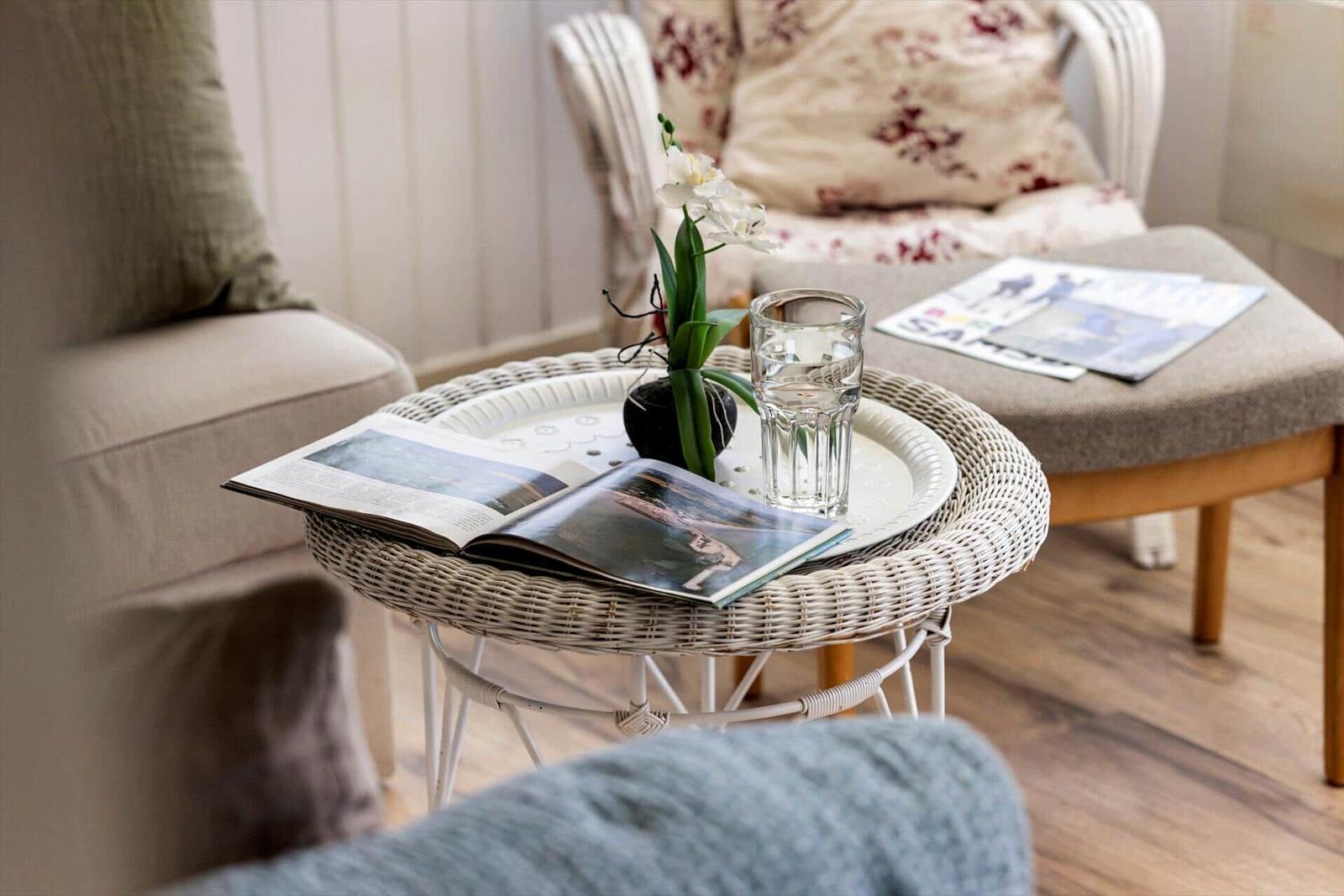 Runder Rattan-Tisch mit Glas, Blume und Zeitschriften im Wohnbereich.