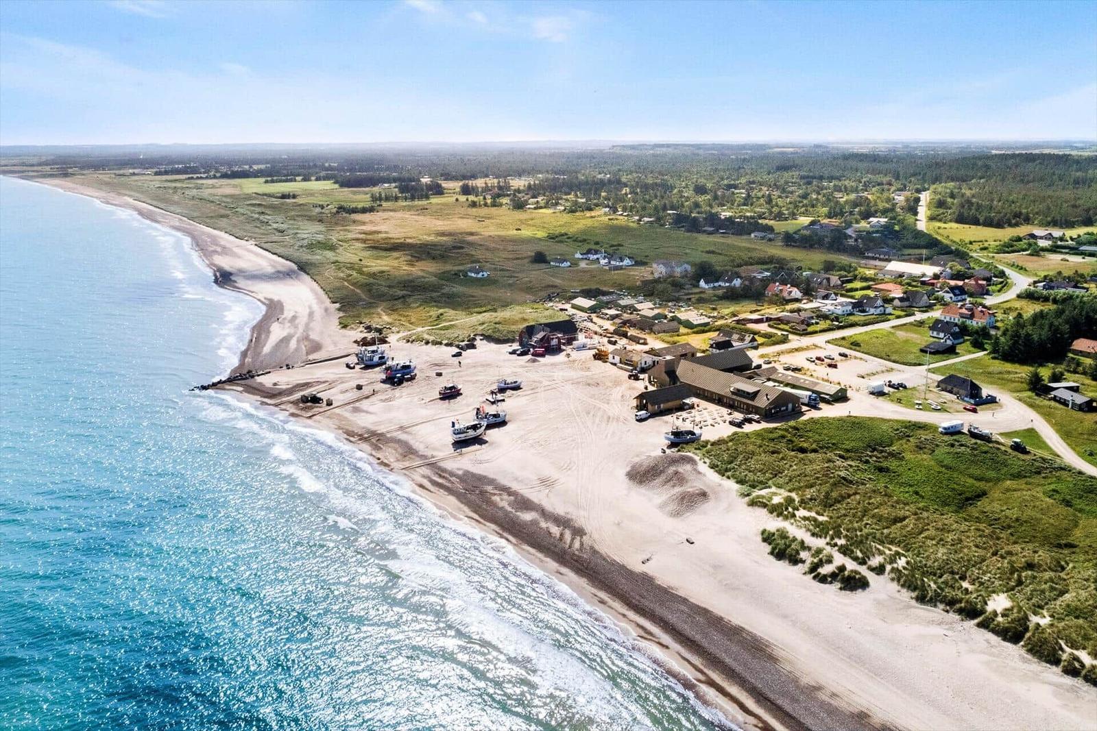 Strandort mit Booten, Häusern und grünen Wiesen am Meer.