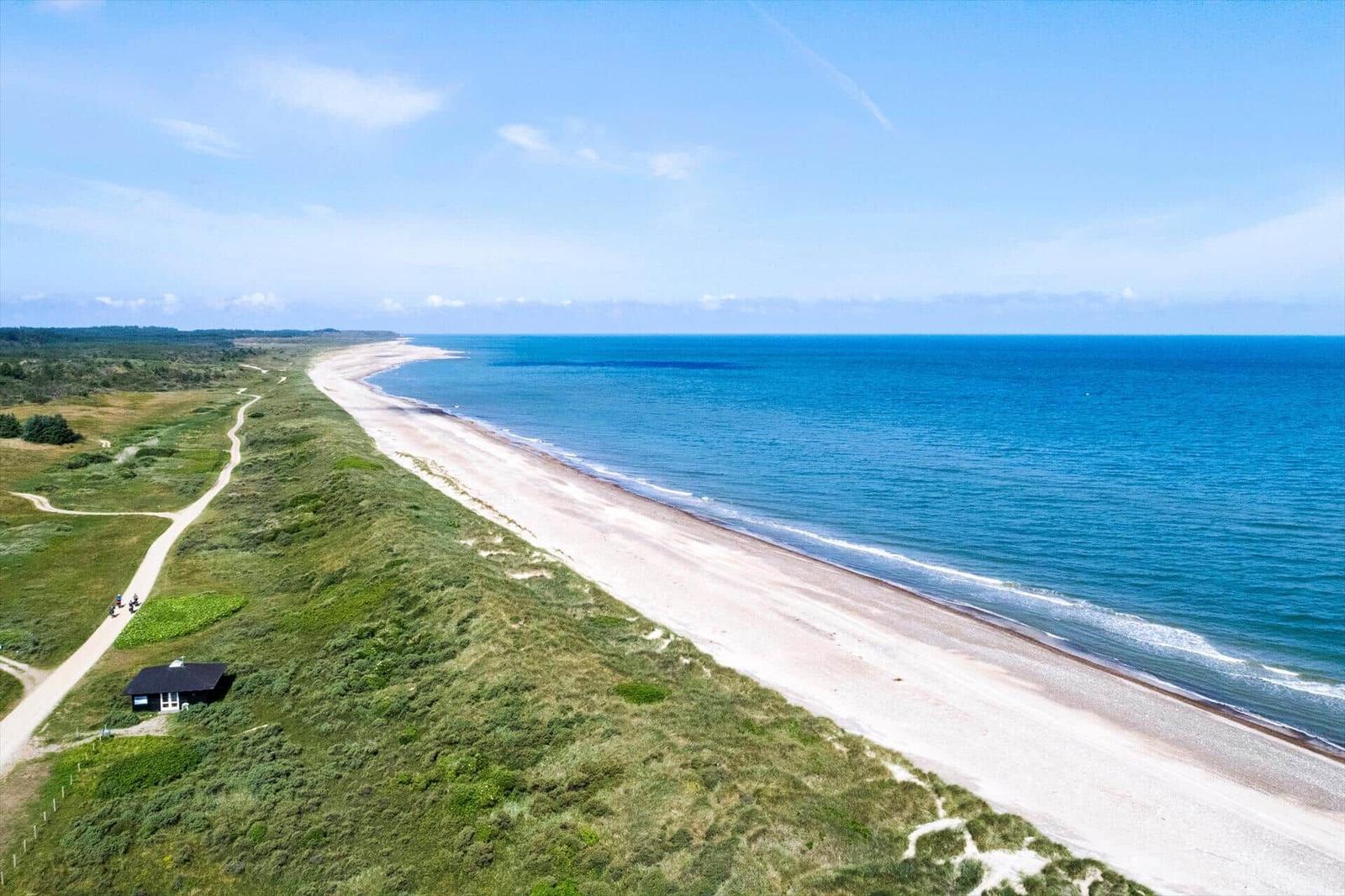 Strandhaus am Meer mit Dünen und Sandstrand unter blauem Himmel