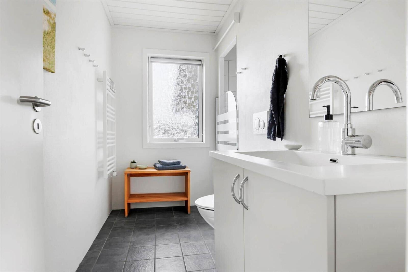 Bathroom with sink, mirror, toilet, and wooden bench.