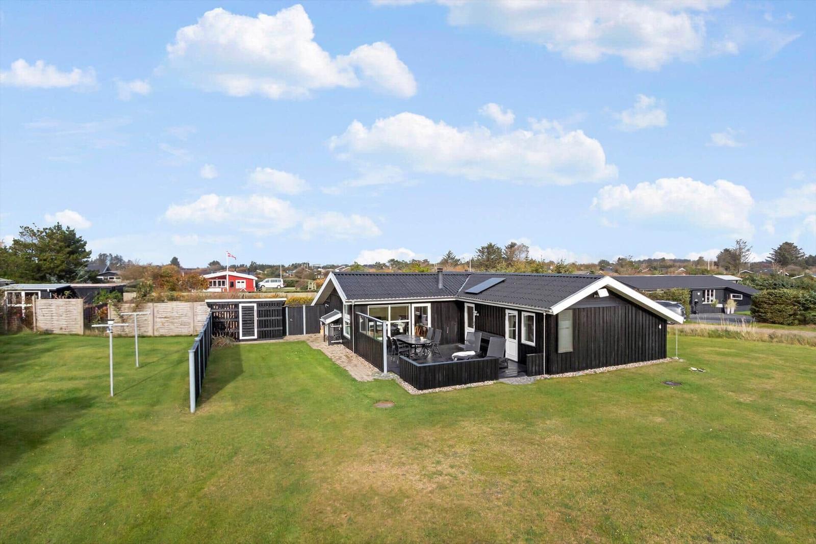 Black wooden house with terrace and garden under blue sky.