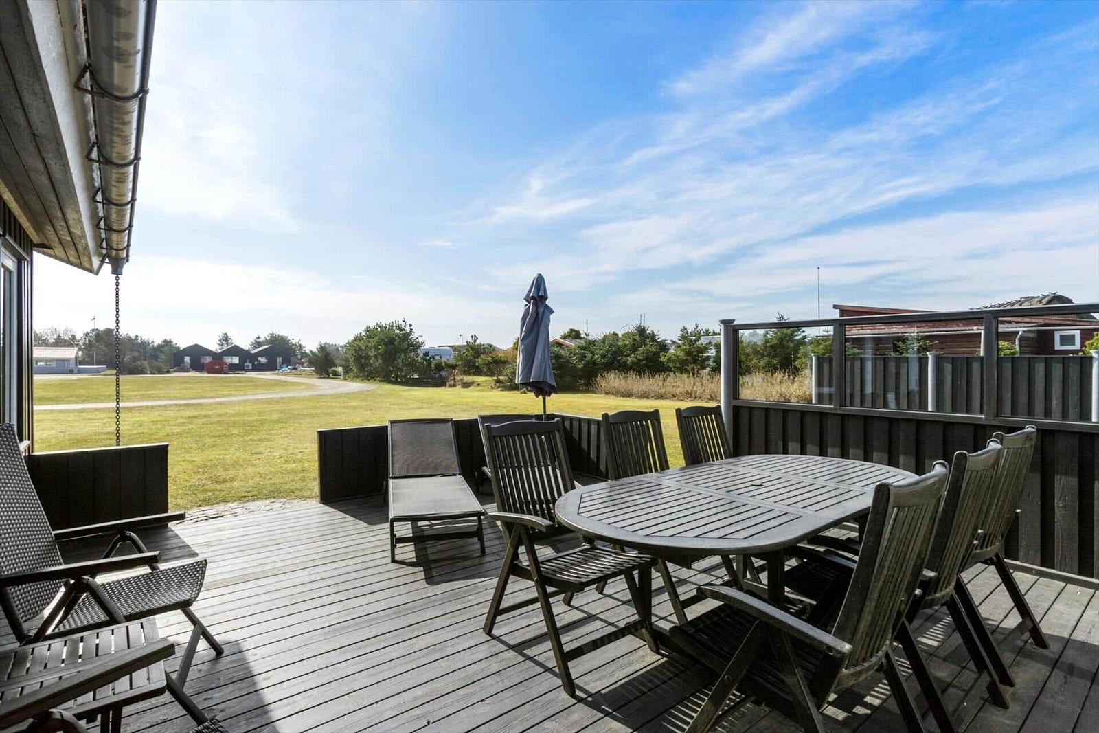 Deck with table, chairs, and umbrella. View of grass field and trees.