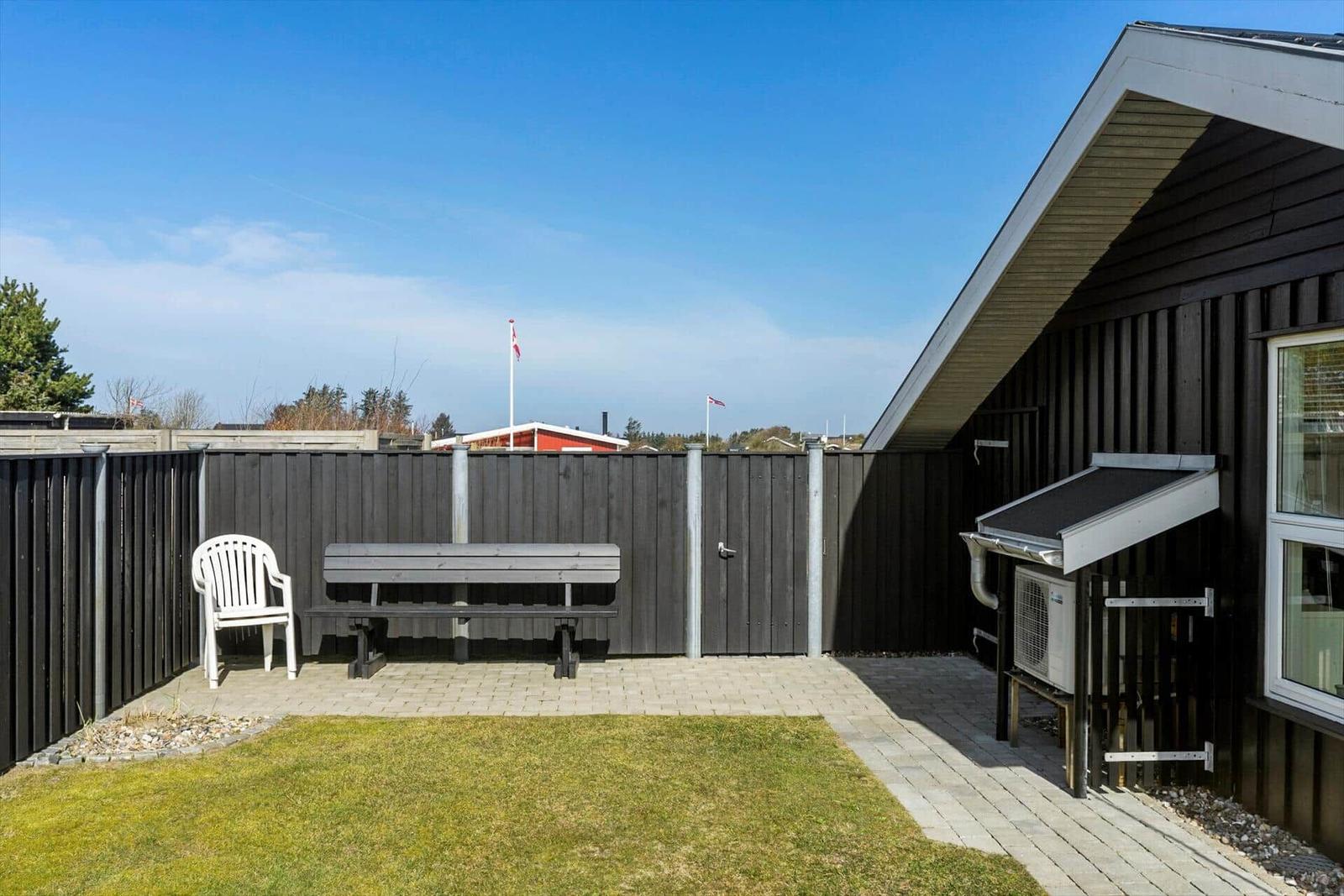 Backyard with bench, chair, and grass area next to dark wood house.