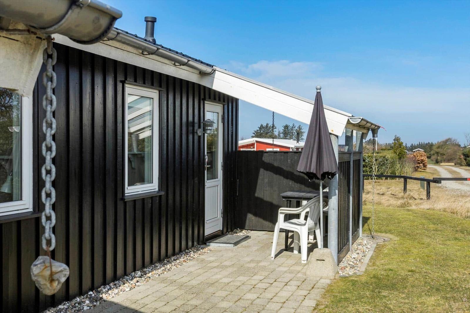 House with balcony, table, chairs, and umbrella. Outdoor area with lawn and fence.