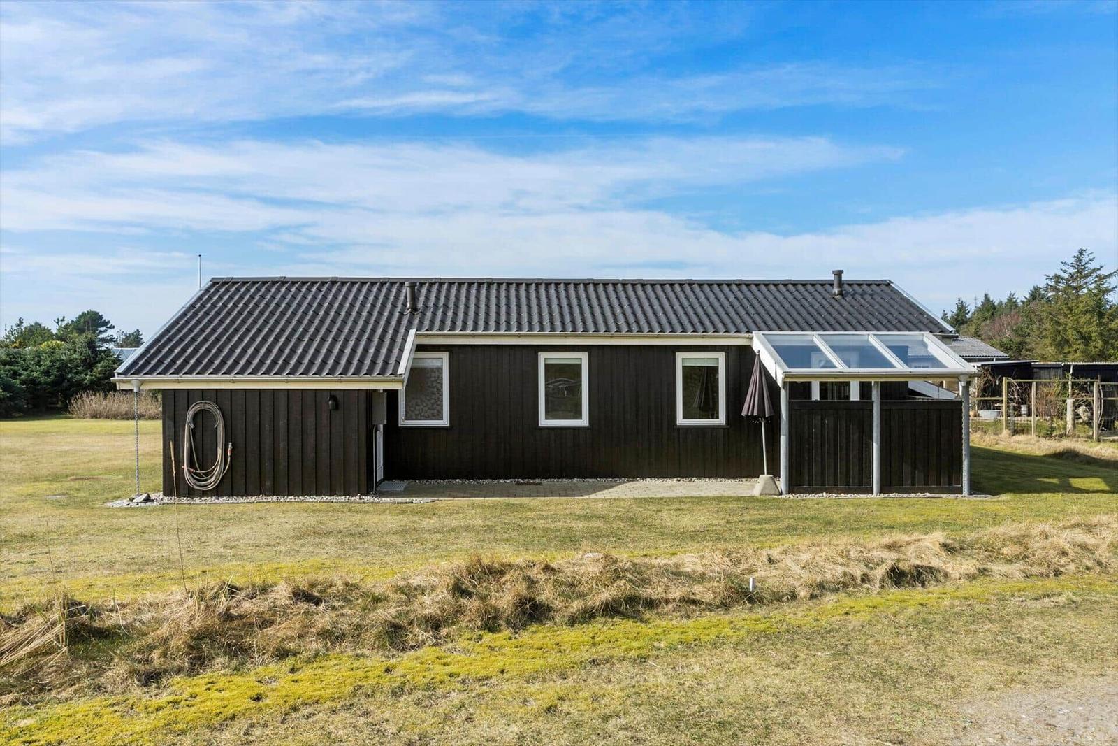 A dark wooden house with roof and glass veranda on green ground.