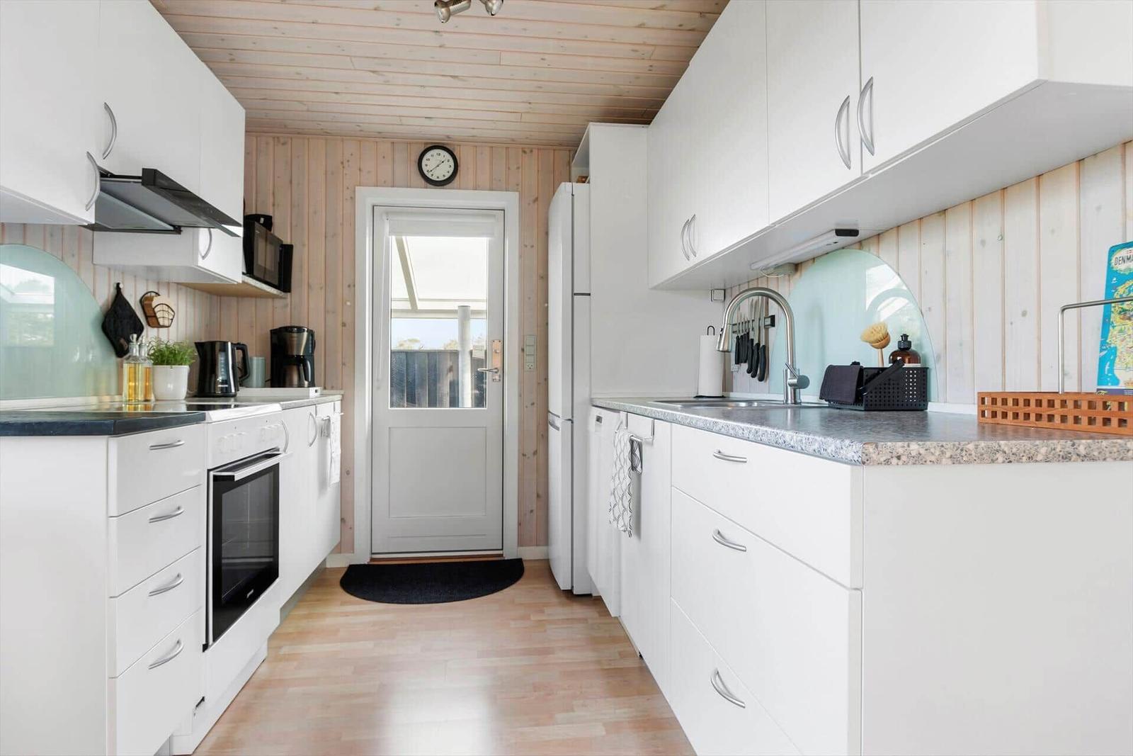 Kitchen with white cabinets, granite countertop, and wooden wall cladding. Door leads to balcony.