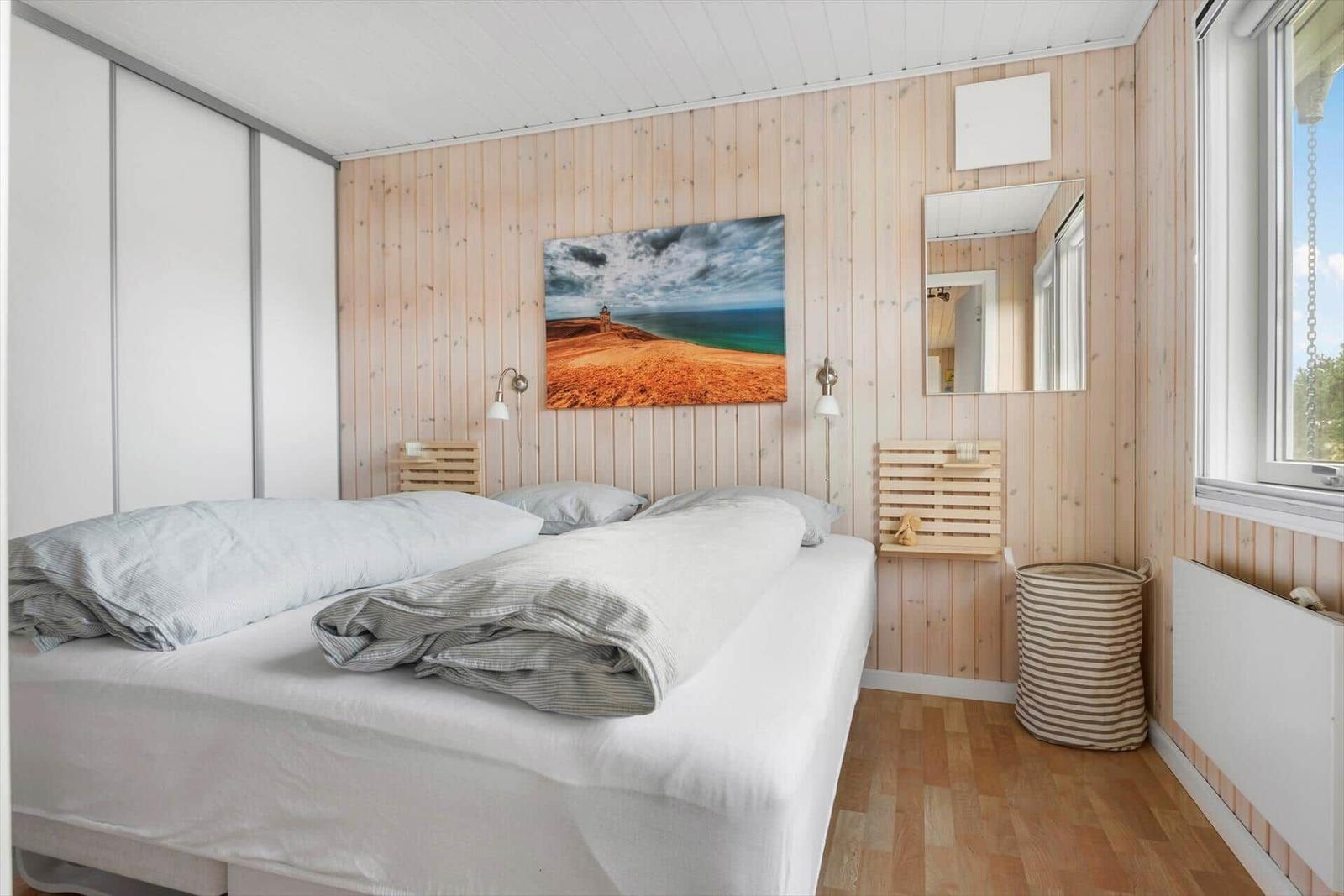 Bedroom with wooden wall, bed, and wall art. Window and mirror visible.