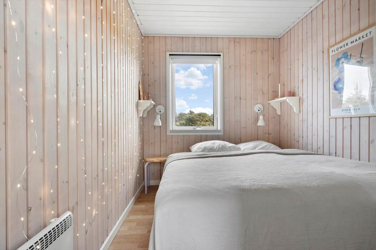 Bedroom with wooden walls, bed, window, and string lights.