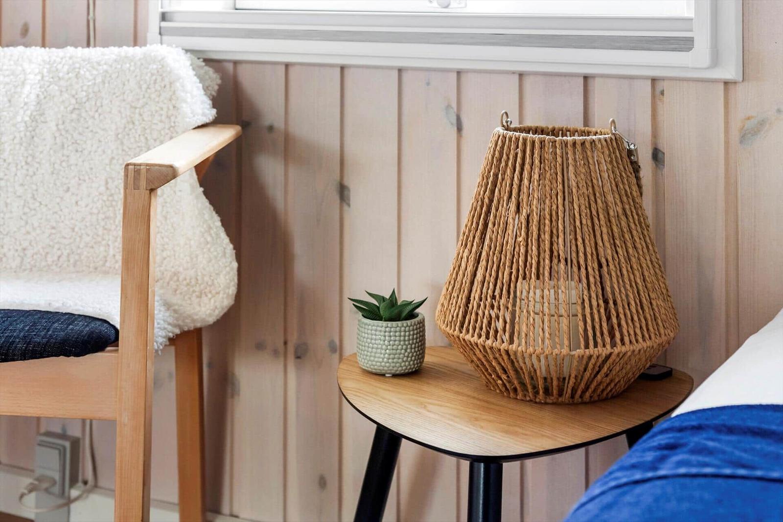 Wooden table with wicker lamp and plant beside chair with blanket.