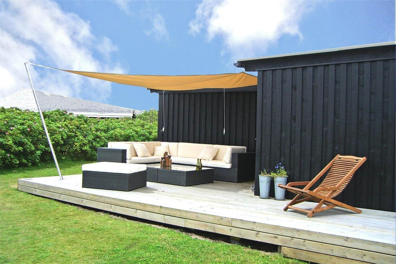Terrasse mit Sitzgruppe, Sonnensegel und Liegestuhl vor schwarzem Holzhaus.