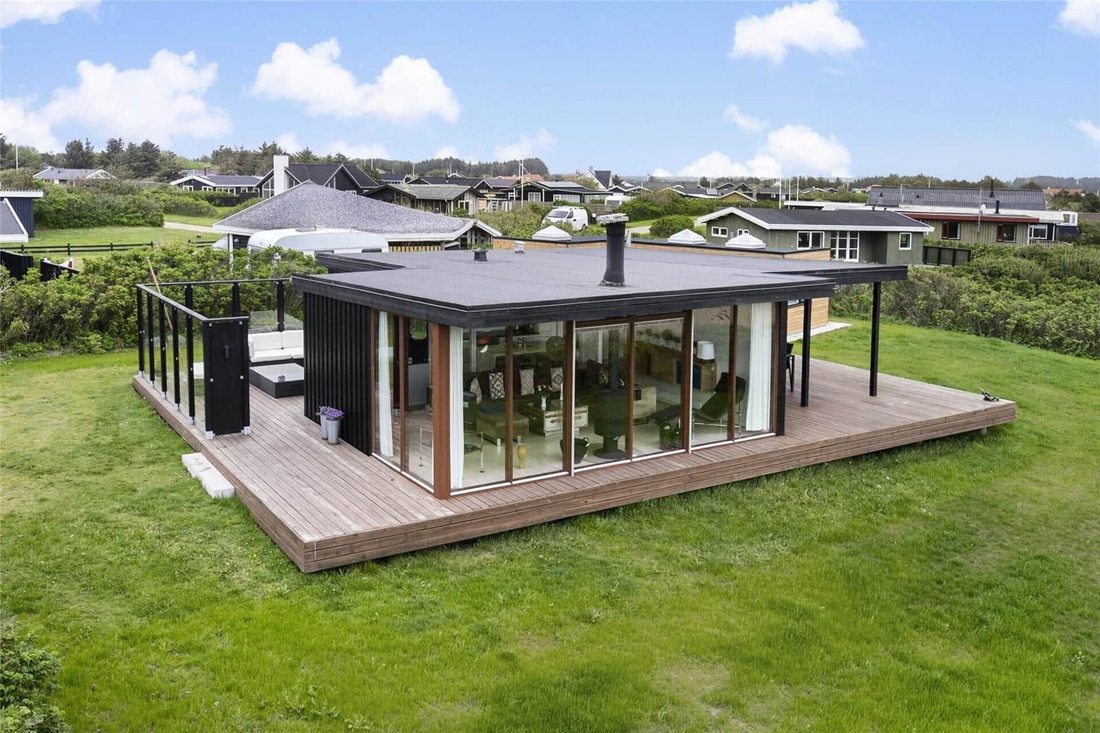Moderne Villa mit großem Holzdeck und Glasfassade. Grünfläche und Blick auf Wohnhäuser.