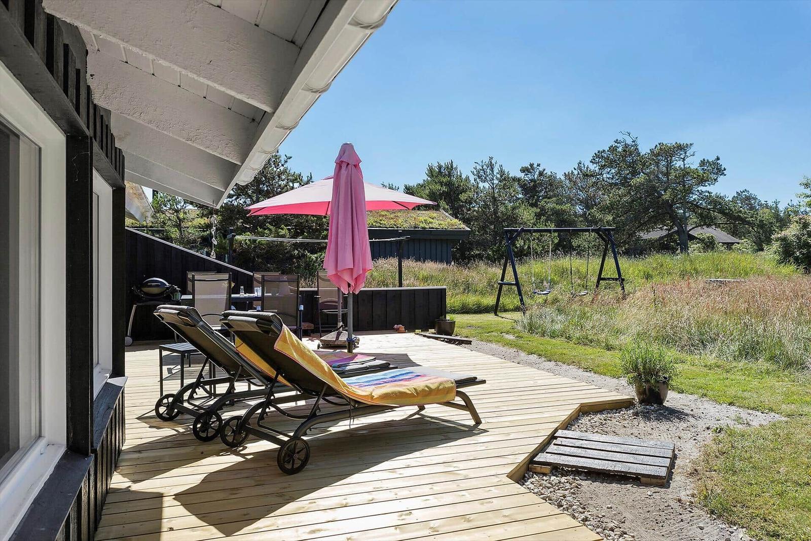 Terrasse mit Liegestühlen, Sonnenschirm und Grill. Hinterhof mit Schaukel und Grünfläche.