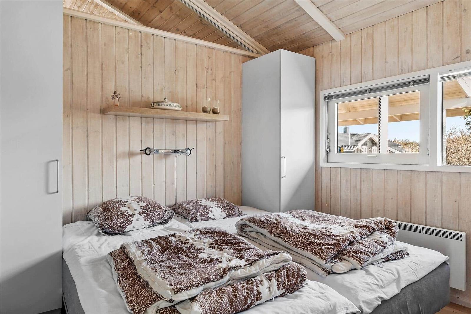Schlafzimmer mit Holzwand, Bett und Fenster