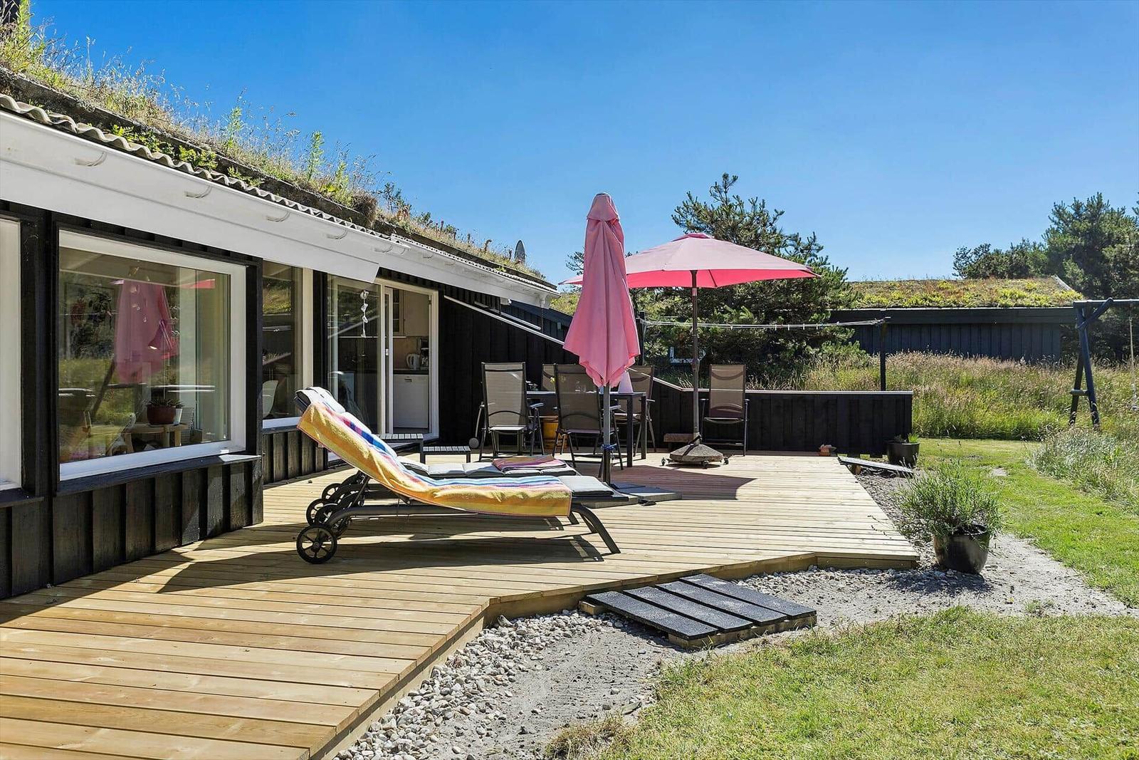 Terrasse mit Liegestuhl, Tisch und Stühlen sowie pinken Sonnenschirmen.