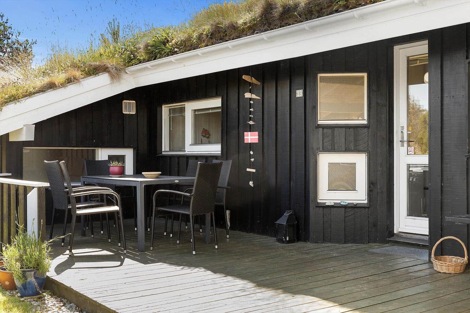 Schwarzes Haus mit grünem Dach, Terrasse mit Tisch und Stühlen, Eingangstür und Fenster.