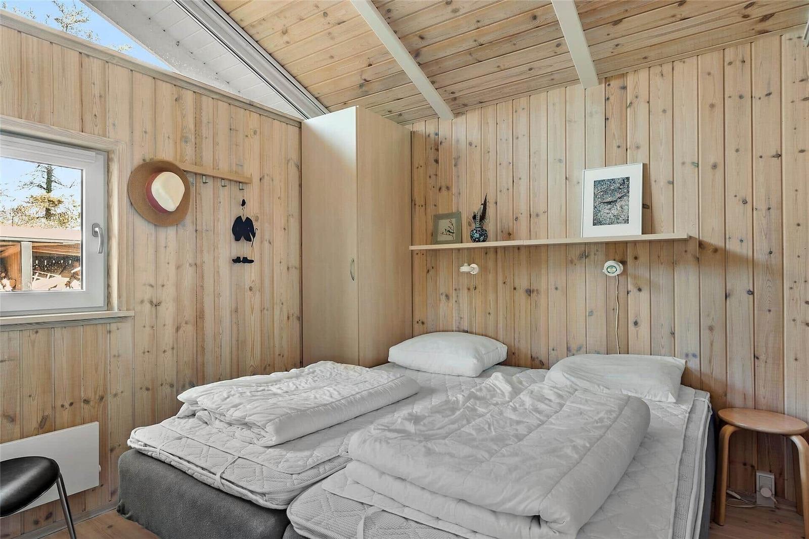 Schlafzimmer mit zwei Betten, Holzwand und Fenster.