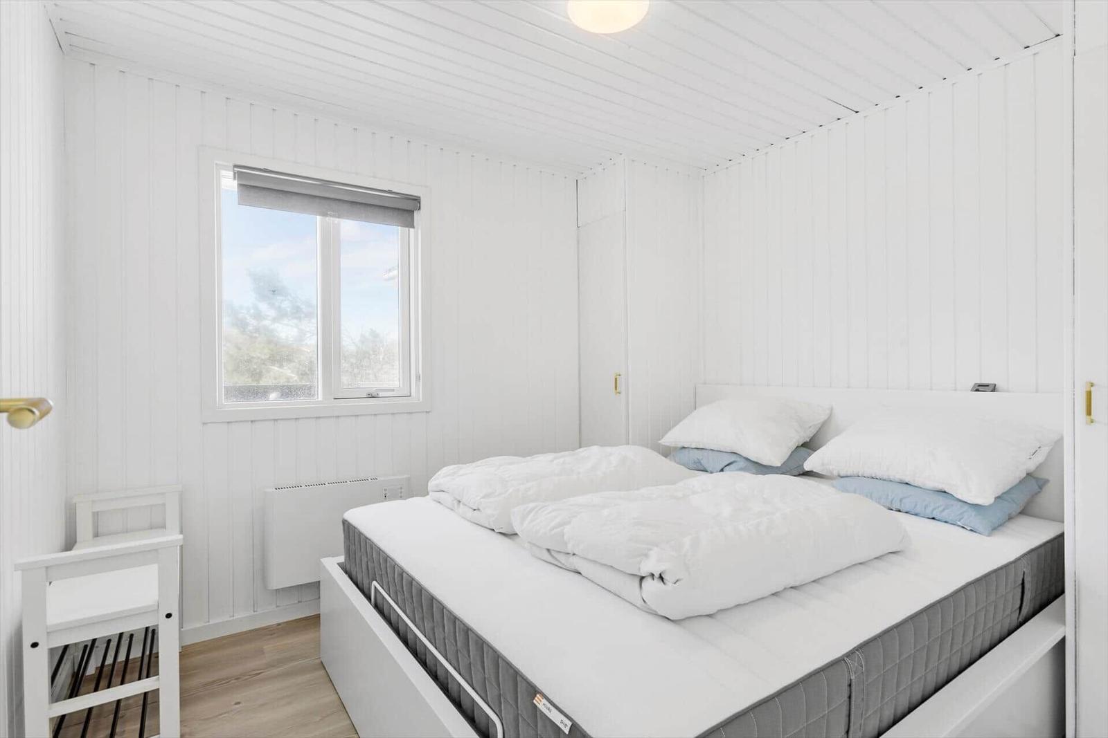 Schlafzimmer mit weißem Bett, Fenster und Holzboden.