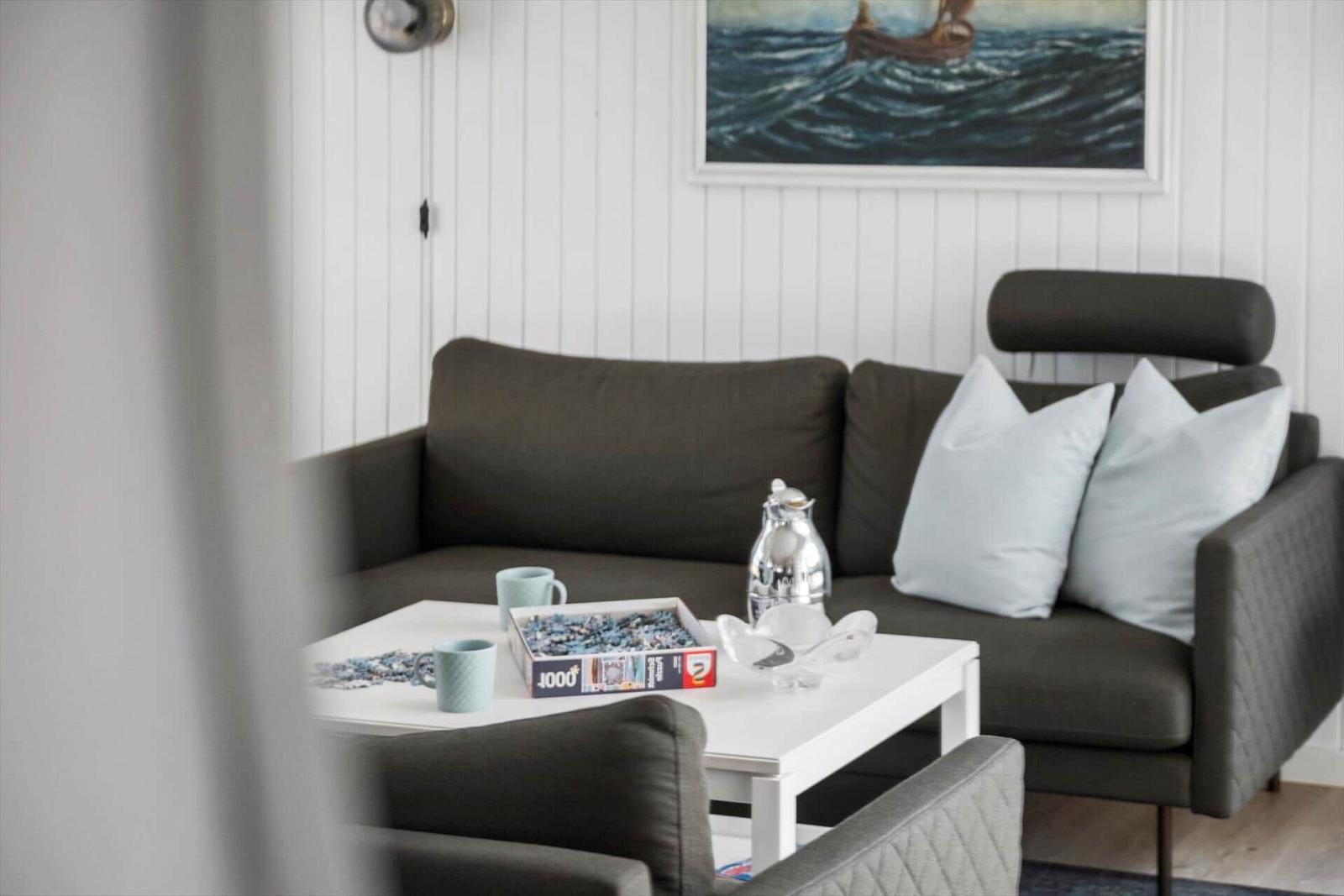 Ein Wohnzimmer mit grauem Sofa, weißem Tisch und Wandbild mit Segelboot.