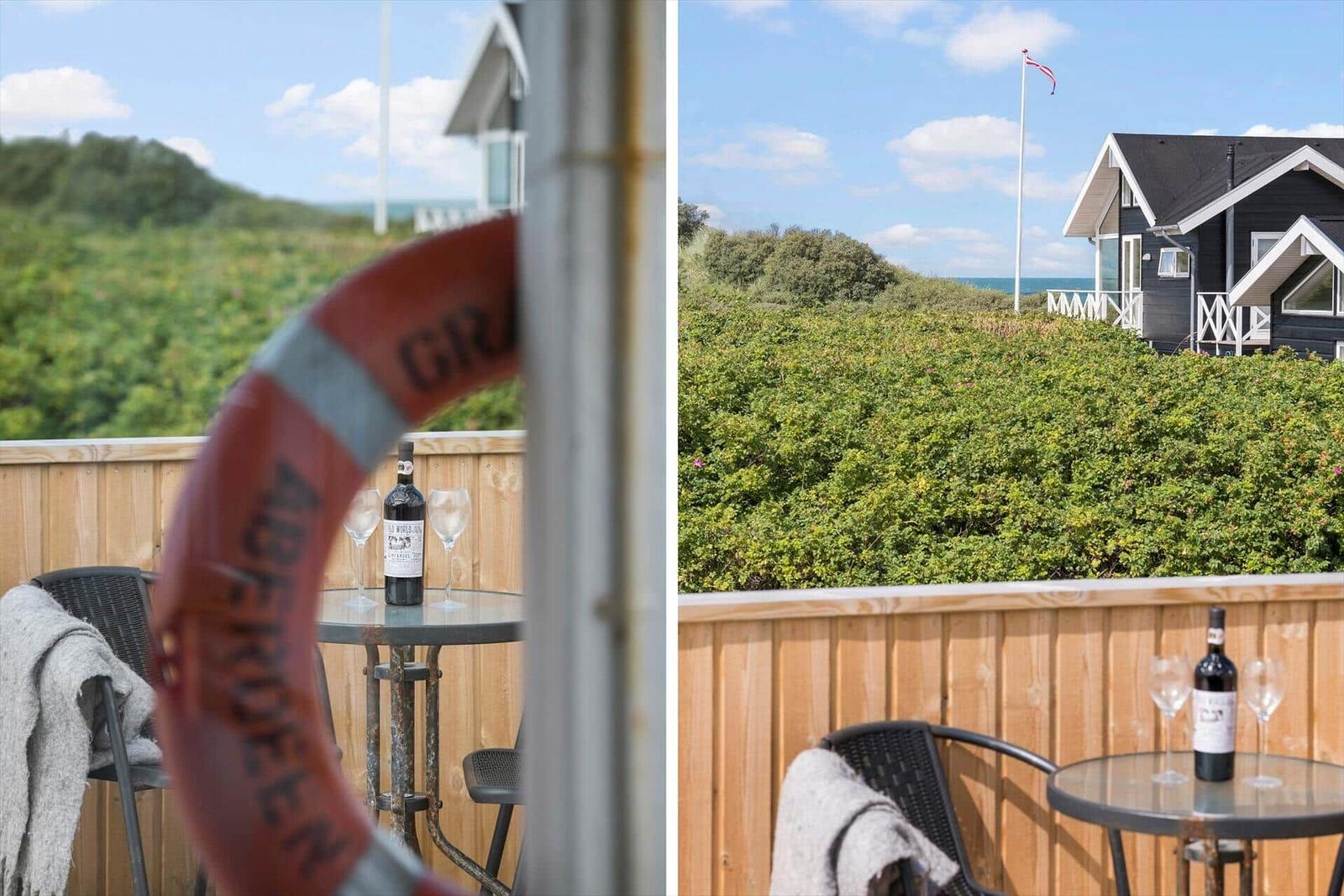 Terrasse mit Tisch, Stühlen und Rettungsring. Blick auf das Haus und den Strand.