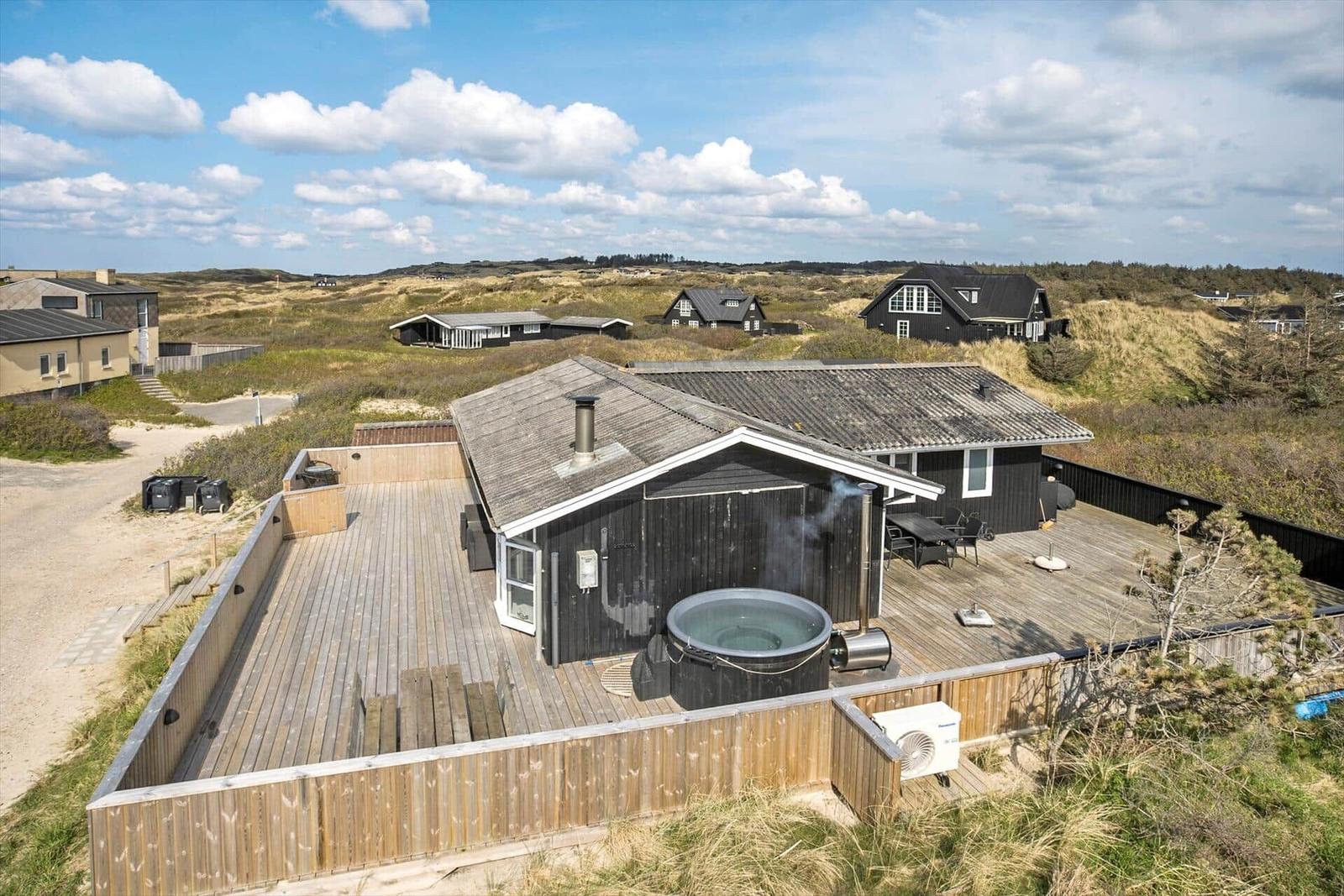 Haus mit Holzterrasse, Whirlpool und Blick auf Dünenlandschaft.