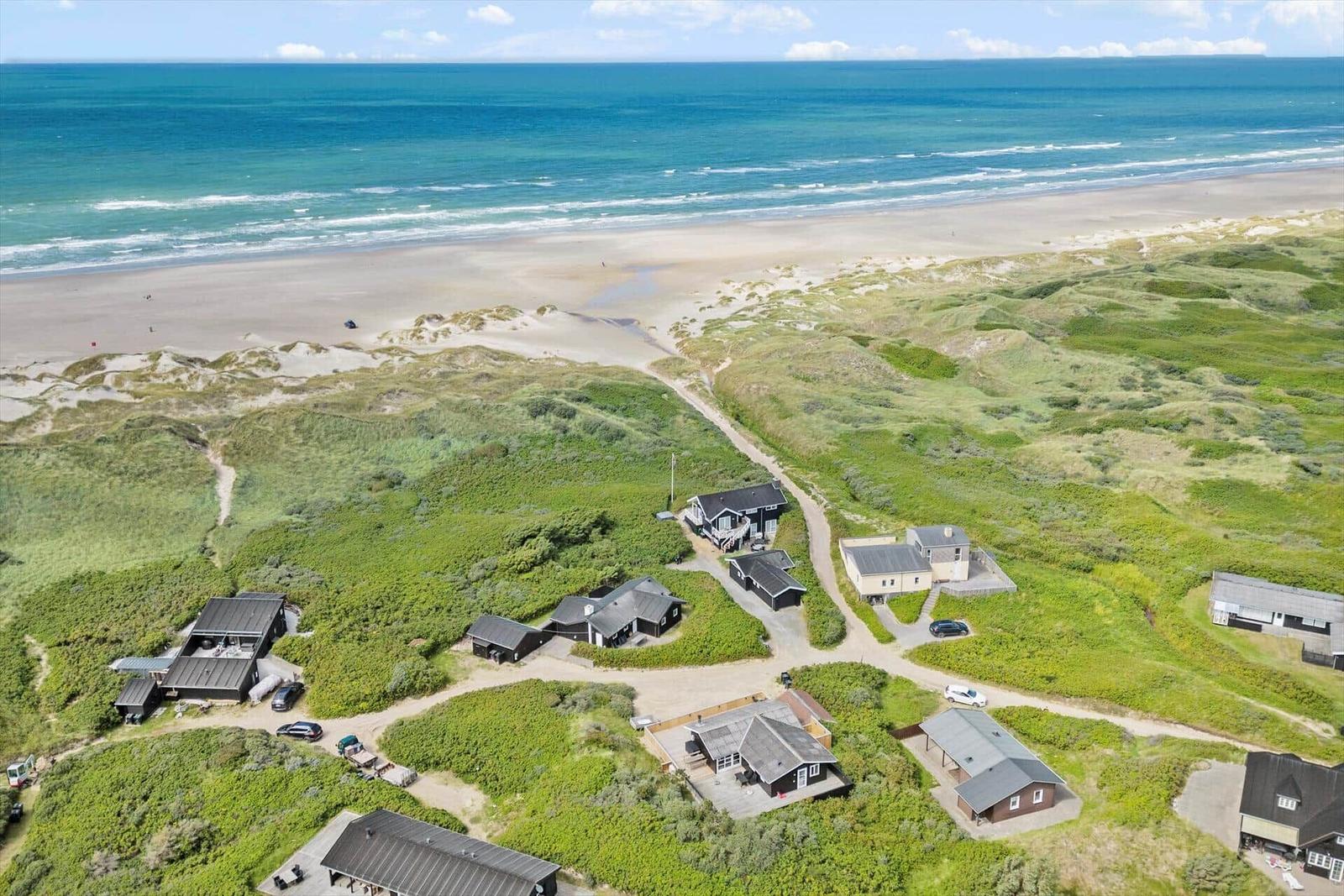 Häuser auf grünen Dünen neben Strand und Meer