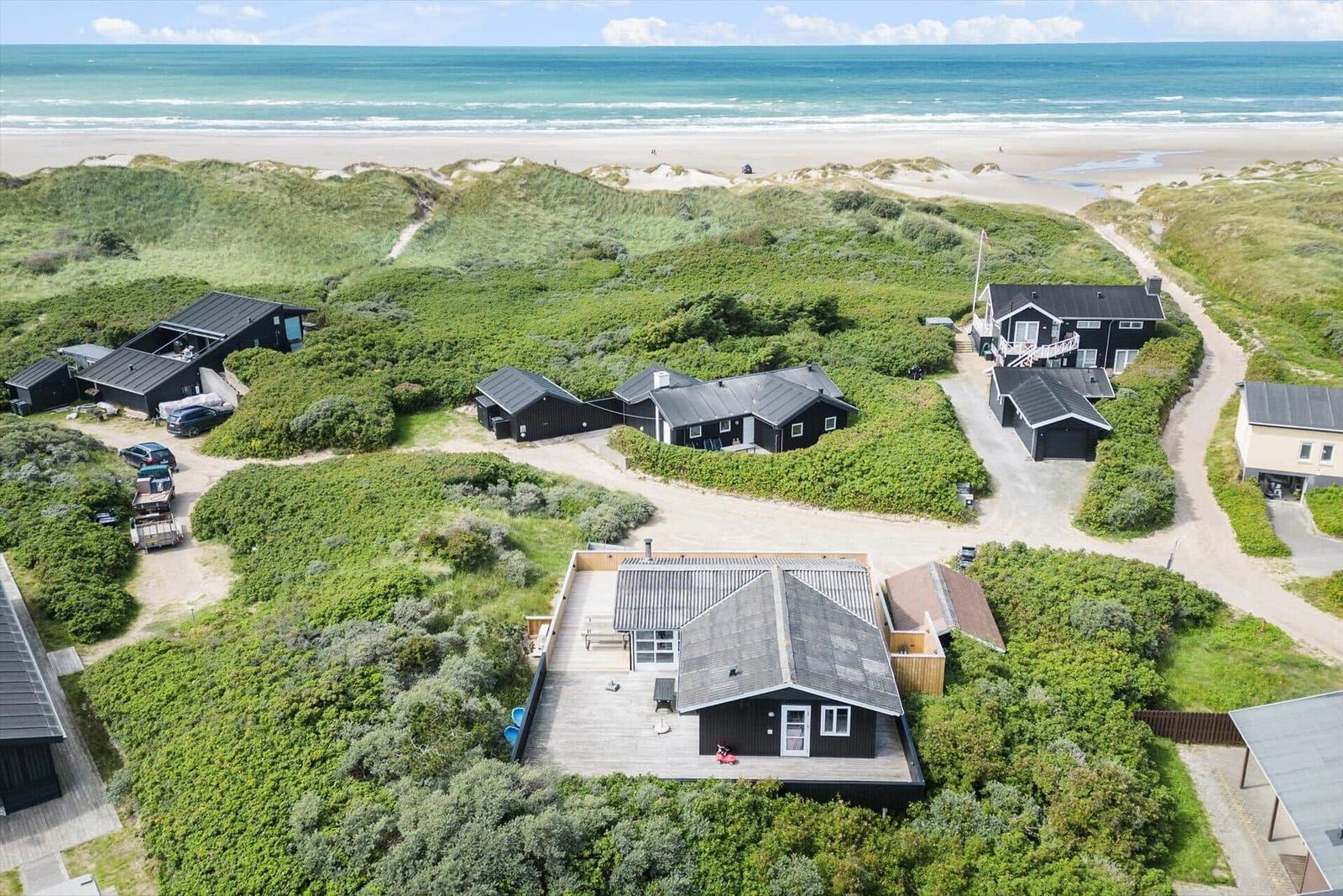 Strandnahe Häuser in grüner Dünenlandschaft mit Meerblick.