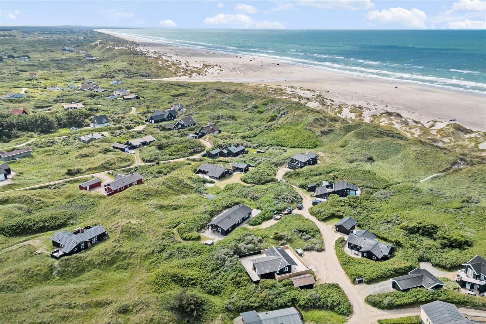 Aussicht auf Strand und Dünen mit mehreren Häusern in der Ferne.
