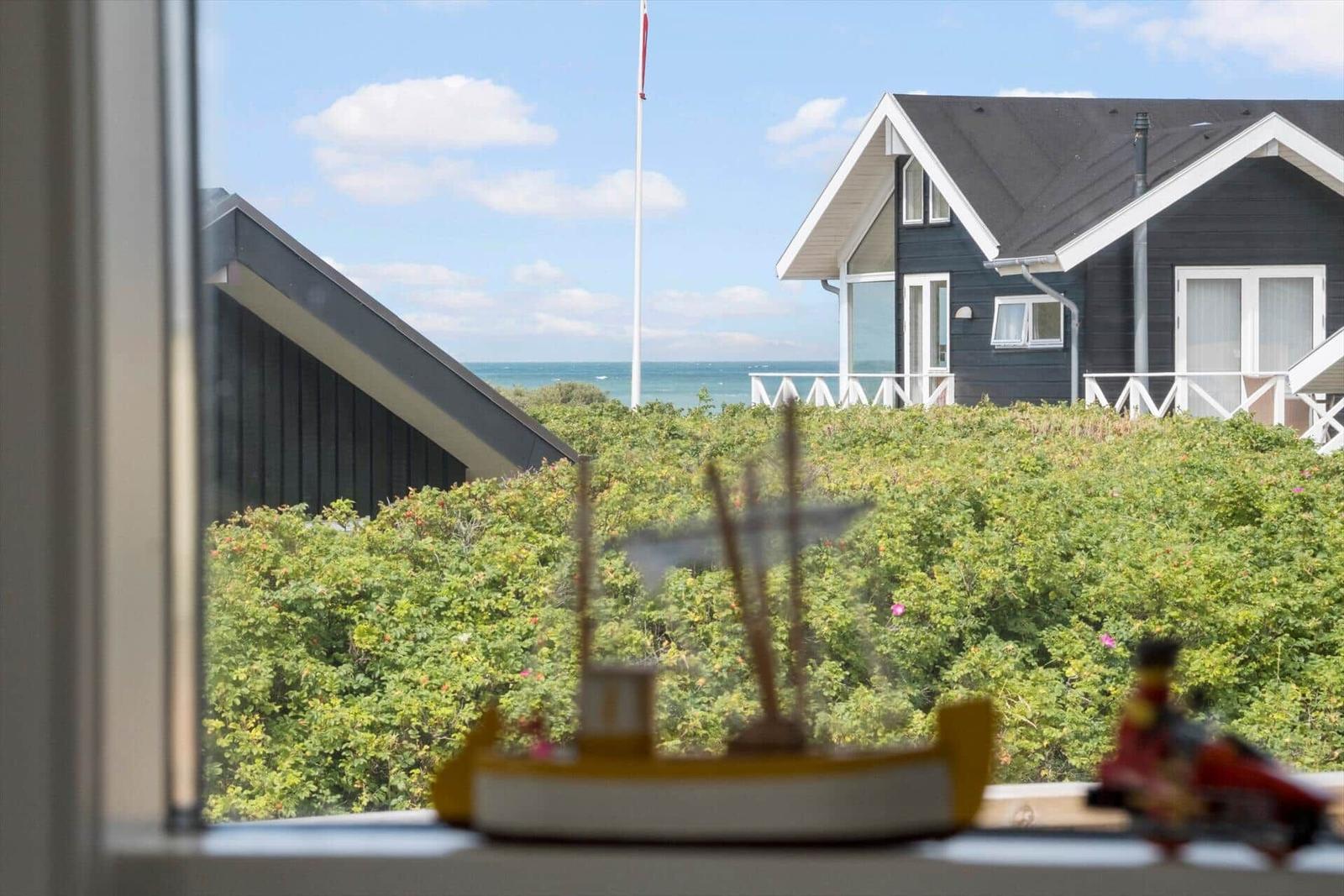 Von Fenster aus Blick auf Strandhaus mit grüner Vegetation und Meer.