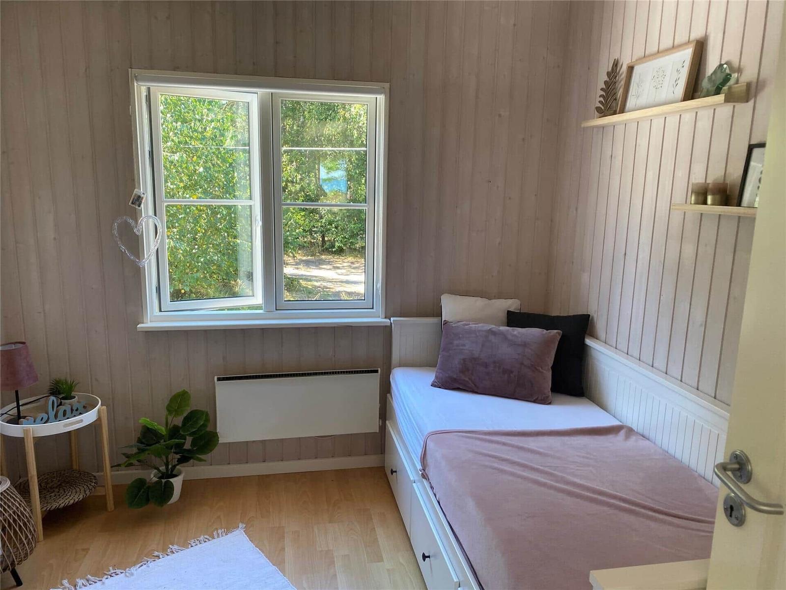 Schlafzimmer mit Bett, Fenster und Holzwand