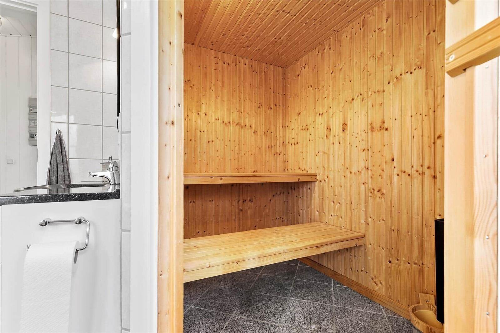 Holzsauna mit zwei Bänken und grauem Bodenbelag. Nebenraum mit Waschbecken und Spiegel.