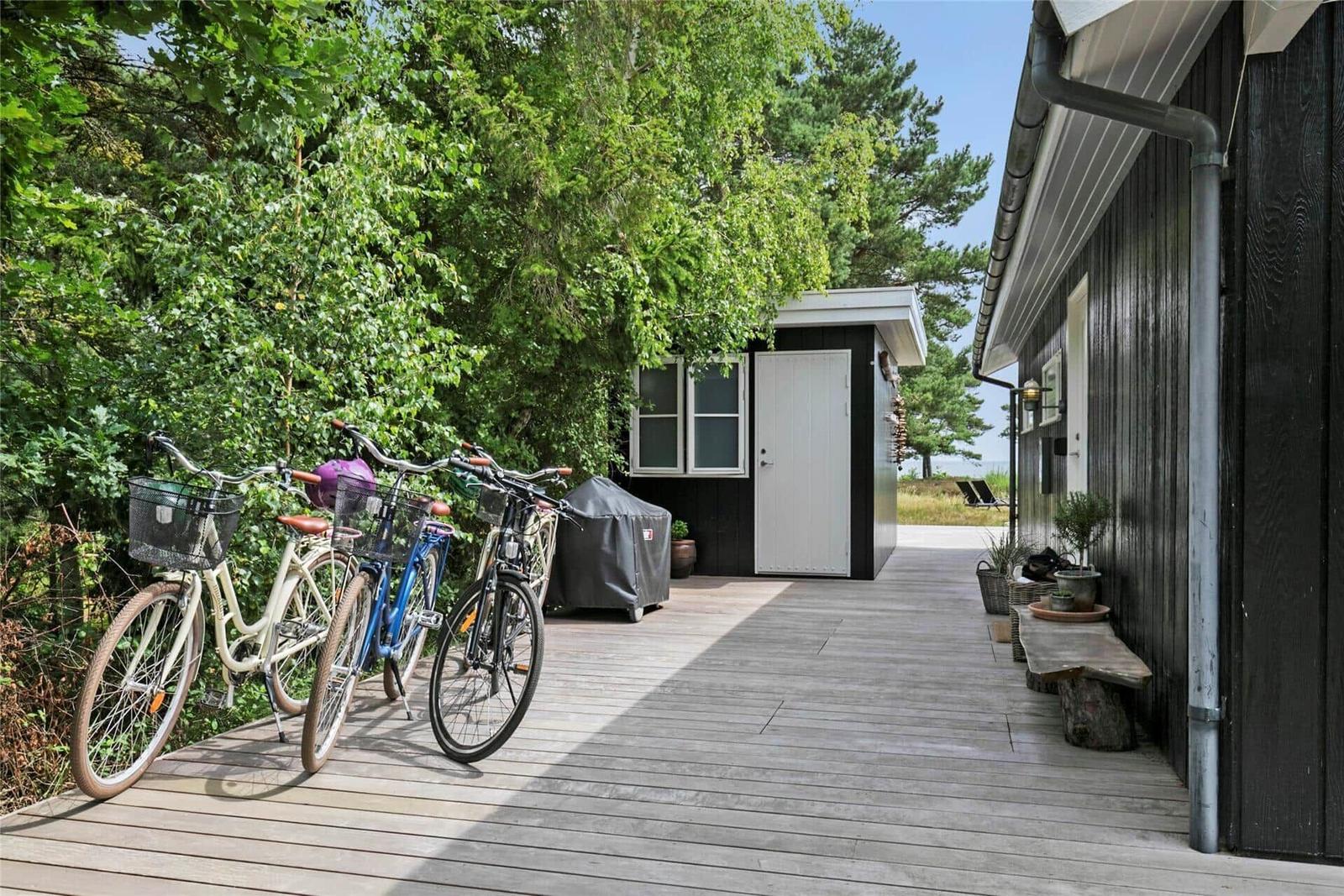 Holzterrasse mit Fahrrädern und kleinem Haus im Grünen.