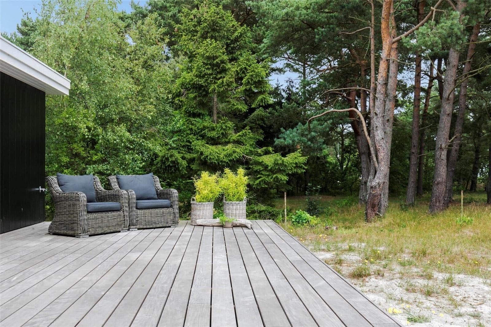 Terrasse mit zwei Sesseln, Pflanzen und Wald im Hintergrund.