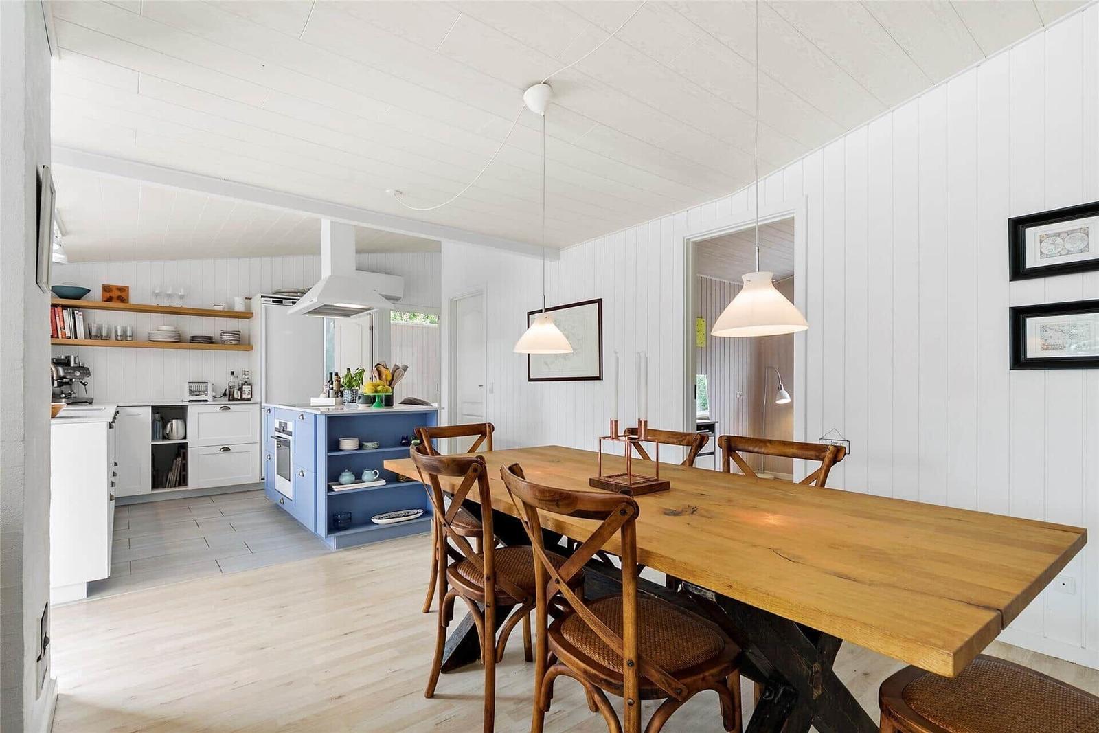 Essbereich mit Holztisch und Stühlen. Küche mit blauer Insel und weißen Wänden.