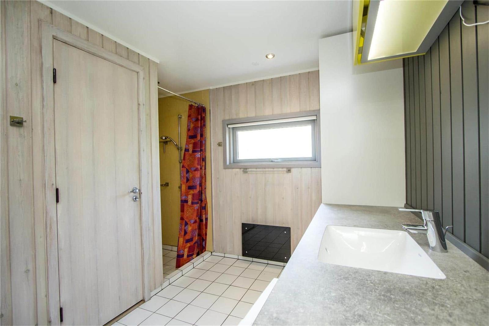 Badezimmer mit Dusche, Waschbecken und Fenster.
